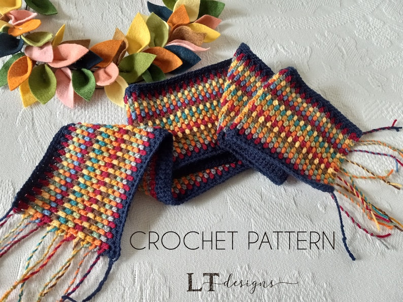May include: A crochet scarf with a multi-colored bobble stitch pattern and navy blue edging. The scarf has long fringe tassels on each end. The text "CROCHET PATTERN LT designs" is visible in the image.