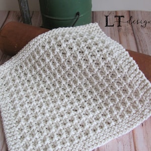 May include: A white knitted dishcloth with a textured pattern. The dishcloth is lying on a wooden surface.