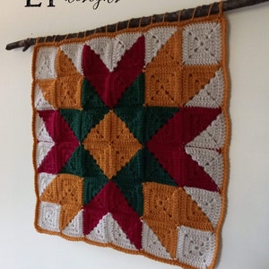 May include: A crocheted wall hanging with a star design in shades of red, green, orange, and white. The hanging is attached to a branch.