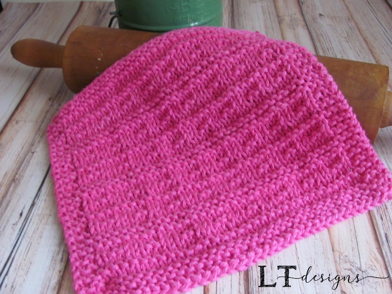 May include: A pink knitted dishcloth with a textured pattern. The dishcloth is made with a soft yarn and is perfect for cleaning dishes or drying hands.