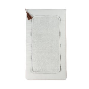 Könnte beinhalten: Eine hellgraue Wickelunterlage mit einem weißen Frottee-Einsatz und einem braunen Quasten. Die Wickelunterlage ist aus einem weichen, gesteppten Stoff.