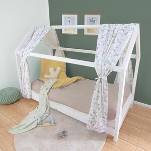 Könnte beinhalten: Weißer, hausförmiger Bettrahmen aus Holz mit einem weißen und grünen gemusterten Baldachin. Das Bett ist mit einer beigefarbenen Bettdecke und einem gelben Kissen bezogen. Eine grün-weiß gemusterte Decke liegt am Fußende des Bettes.