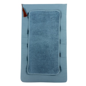 Könnte beinhalten: Eine hellblaue Wickelunterlage mit einem weichen, strukturierten, blauen Handtucheinsatz. Die Unterlage hat einen braunen Quasten an der oberen linken Ecke.