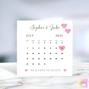 Może przedstawiać: Biała kartka z kalendarzem na lipiec 2024. Data 13 lipca jest zakreślona r&oacute;żowym sercem. Na kartce widnieje tekst "Sophie & Luke" i "WE'D LOVE TO ACCEPT".