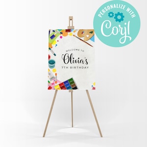 May include: A wooden easel holds a birthday sign with the text "Welcome to Olivia's 7th Birthday." The sign is decorated with colourful art supplies, including paint tubes, paint palettes, and watercolour paints. A teal circle with the text "Personalize with Corjl" is in the upper right.