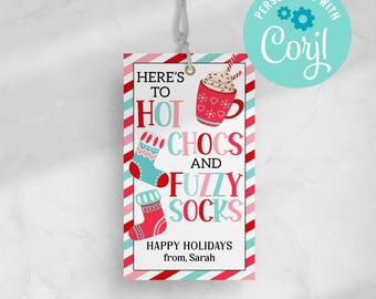 Pode incluir: Uma etiqueta de presente listrada de vermelho e branco com uma meia listrada de azul e branco, uma meia vermelha e uma caneca de chocolate quente com chantilly e granulado. O texto na etiqueta diz "Here's to hot chocs and fuzzy socks. Happy Holidays from, Sarah."