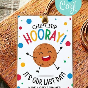 Puede incluir: Una etiqueta de regalo rectangular blanca con un ojal de latón y cordel marrón. La etiqueta presenta una galleta con chispas de chocolate sonriente, puntos de colores y el texto: CHIP CHIP HOORAY! IT'S OUR LAST DAY! HAVE A GREAT SUMMER! from Emily.
