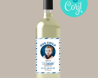 Könnte beinhalten: Eine klare Weinflasche mit schwarzem Verschluss und individuellem Etikett. Das Etikett zeigt ein Foto eines Kindes, die Worte "OUR CHILD" und den Text "might be the reason you drink so please enjoy this little one! Happy Holidays".