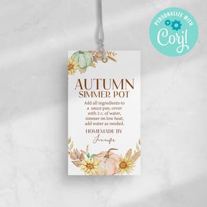 以下が含まれることがあります： 「AUTUMN SIMMER POT」のテキストと使用方法が記載された長方形のタグ。カボチャ、ヒマワリ、葉のイラストが水彩画で描かれています。タグは灰色の紐で吊り下げられています。