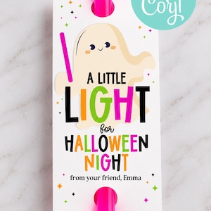 May include: A white rectangular gift tag featuring a cartoon ghost and the text A LITTLE LIGHT for HALLOWEEN NIGHT from your friend, Emma. The tag is accented with colorful stars and held by a bright pink plastic clip at the top and bottom.