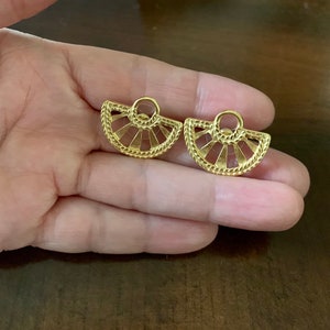 Op de afbeelding: Een paar goudkleurige oorbellen. Elke oorbel heeft een waaiervormig ontwerp met een getextureerde rand en een kleine lus aan de bovenkant. De oorbellen worden op een hand getoond.