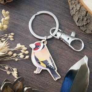 a wooden charm keyring with a swivel clasp shaped and illustrated as a goldfinch bird