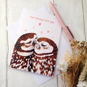 a cream a6 size card with two illustrated little owls snuggling with pink hearts above them with the words owl always love you written above them in pink. the card is sat on a white envelope