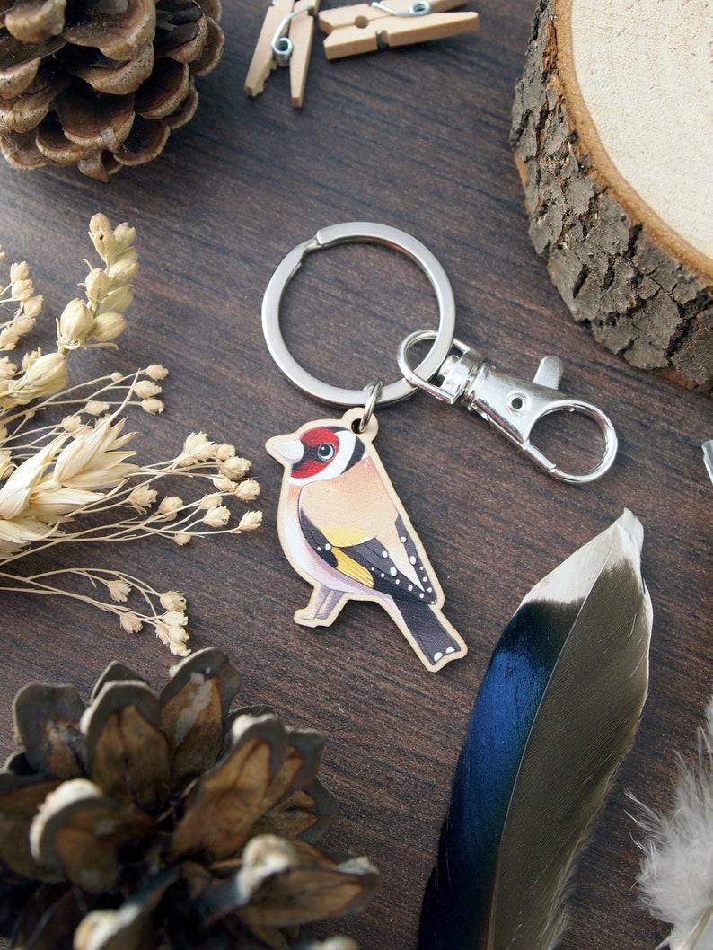 a wooden charm keyring with a swivel clasp shaped and illustrated as a goldfinch bird