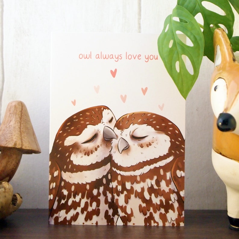a cream a6 size card with two illustrated little owls snuggling with pink hearts above them with the words owl always love you written above them in pink. the card is standing on a shelf