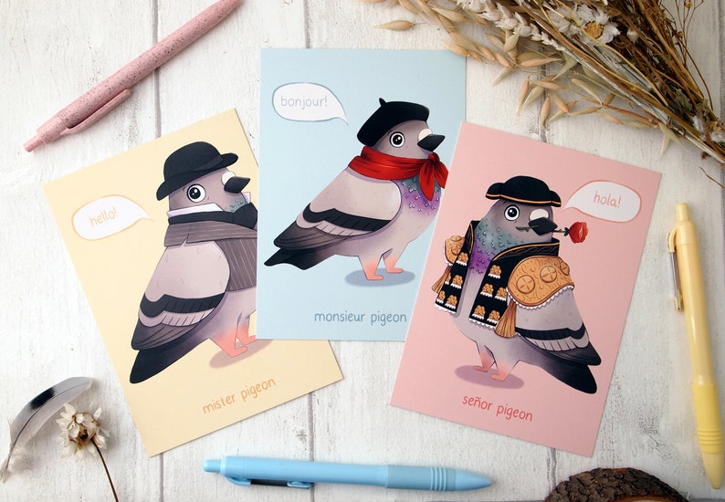 A set of three A6 size postcards all with illustrated pigeons, one wearing a bowler hat and waistcoat on a yellow background, another wearing a beret and neck scarf on a blue background and the third wearing a matador costume on a pink background