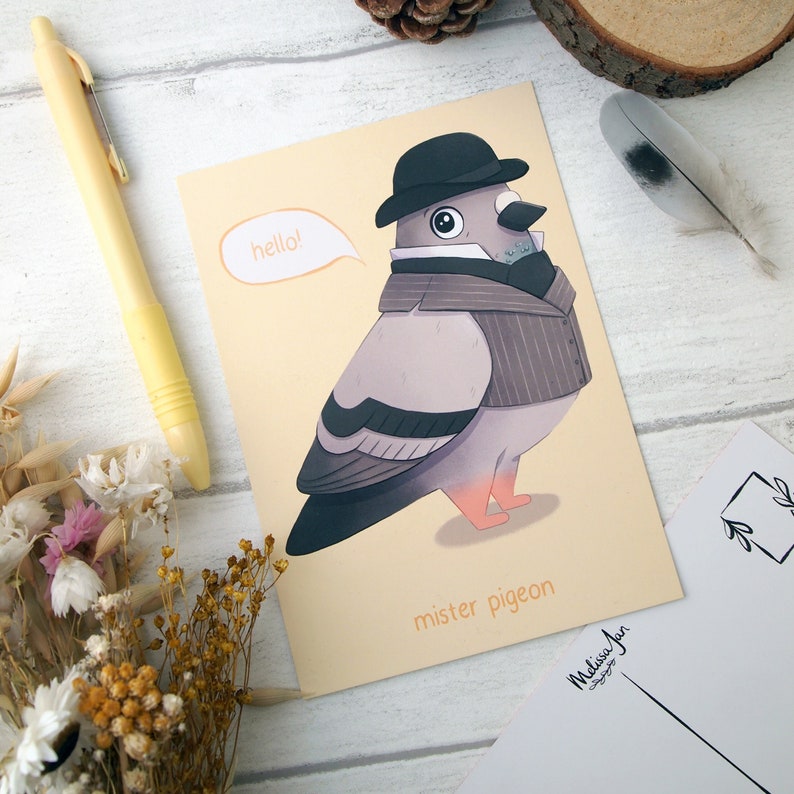 An A6 size postcard with an illustrated pigeon wearing a bowler hat and waistcoat with a speech bubble saying hello and with the words mister pigeon below on a yellow background. The postcard is placed on another postcard showing the back design