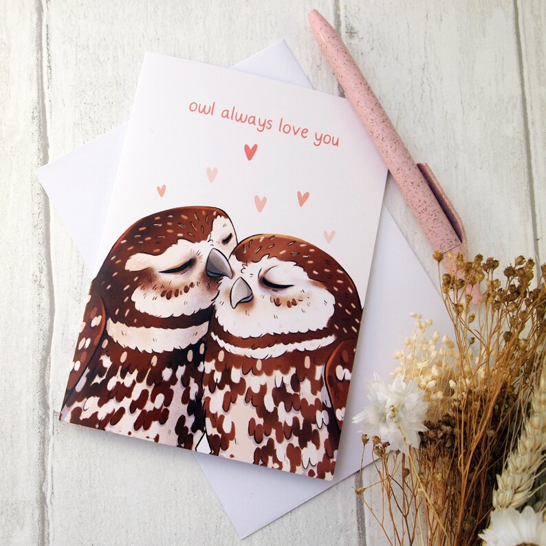 a cream a6 size card with two illustrated little owls snuggling with pink hearts above them with the words owl always love you written above them in pink. the card is sat on a white envelope