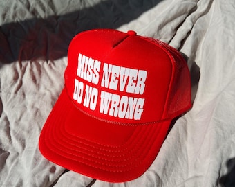 May include: Red trucker hat with a white mesh back. The front of the hat has white text that reads "Miss Never Do No Wrong."