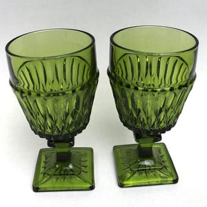 May include: Two green-tinted glass goblets with a textured diamond pattern on the bowl and a square base. The goblets have a unique design with a slightly angled rim and a stem connecting the bowl to the base.