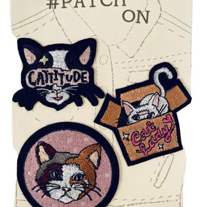 May include: Three embroidered iron-on patches on a display card labeled #PATCH ON. One patch is a black cat head with the text CATTITUDE, one is a calico cat face in a pink circle, and one is a white cat inside a brown box with the text Cat lady.