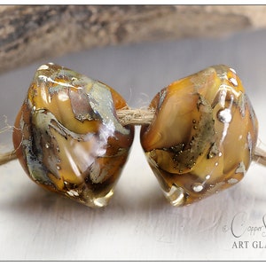 Può includere: Due perline di vetro ambrato con macchie dorate e argentate, infilate su uno spago. Le perline sono sfaccettate e hanno una forma leggermente irregolare. Le perline sono di Copper Stone Art Glass.
