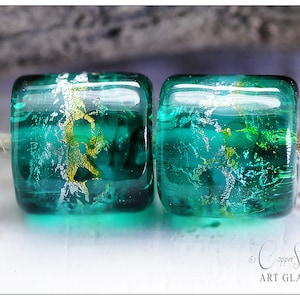 May include: Two teal blue glass beads with gold and silver flecks. The beads are round and have a smooth, shiny surface.