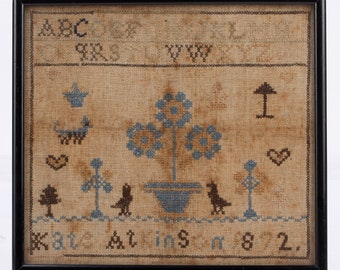 May include: A framed sampler with blue and brown embroidery depicting a tree, birds, and a heart. The sampler includes the letters ABC and the text "Done at 182."
