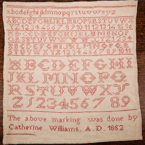 Könnte beinhalten: Ein Stickmuster mit roten gestickten Buchstaben des Alphabets, Zahlen und dem Text "The above marking was done by Catherine Williams. A.D. 1852".