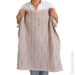 Puede incluir: Una manta de ganchillo beige con un patr&oacute;n vertical repetitivo de puntos en relieve en forma de hoja, separados por columnas de puntos altos. El tejido tiene una superficie texturizada y un color tostado claro uniforme en toda la pieza.