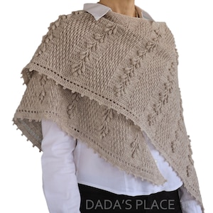 May include: A beige crocheted shawl with a delicate leaf pattern and a scalloped edge. The shawl is draped over a person's shoulders and is worn with a white shirt and black pants. The text "DADA'S PLACE" is visible in the bottom right corner of the image.