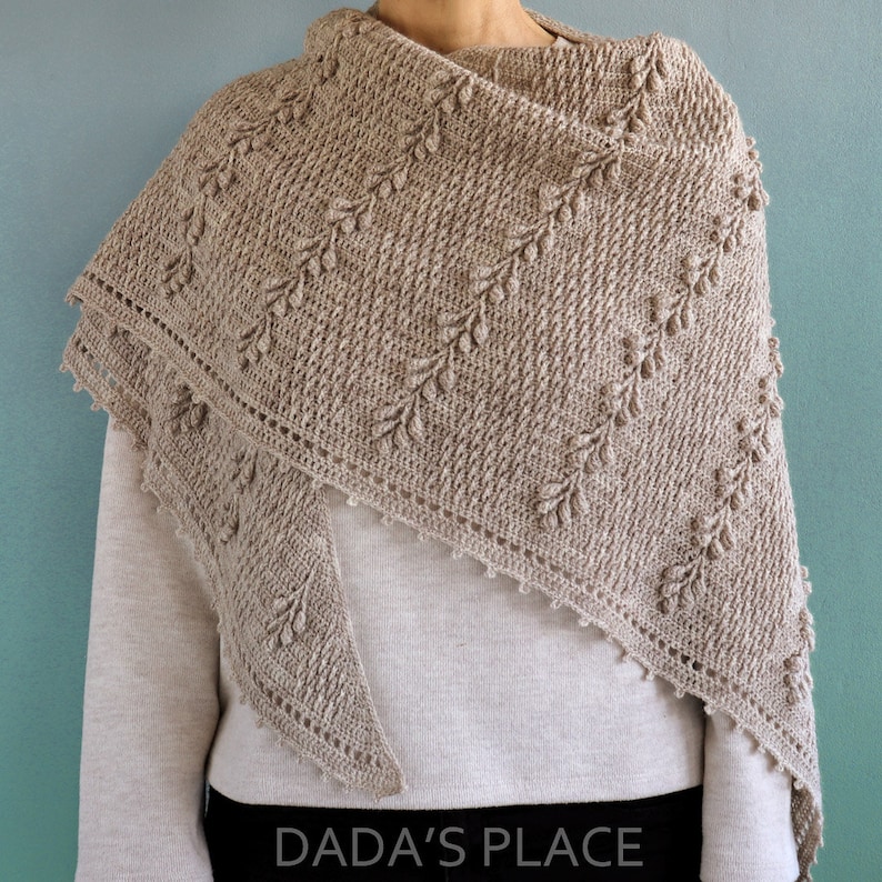 May include: A beige crochet shawl with a delicate leaf pattern and a scalloped edge. The shawl is draped over a person's shoulders.