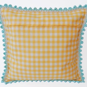 May include: A yellow and white gingham pillow with a blue crocheted border. The pillow has a zipper closure on the back.