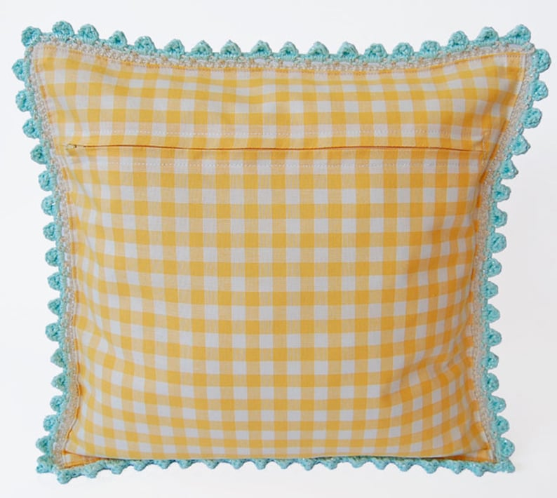 May include: A yellow and white gingham pillow with a blue crocheted border. The pillow has a zipper closure on the back.