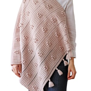Peut inclure: Un ch&acirc;le en crochet rose avec un motif en losange et des glands. Le ch&acirc;le est drap&eacute; sur les &eacute;paules d'une personne.
