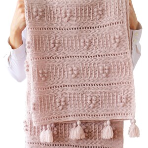 Peut inclure: Une couverture pour b&eacute;b&eacute; en crochet rose avec un motif textur&eacute; et des pompons sur les bords.