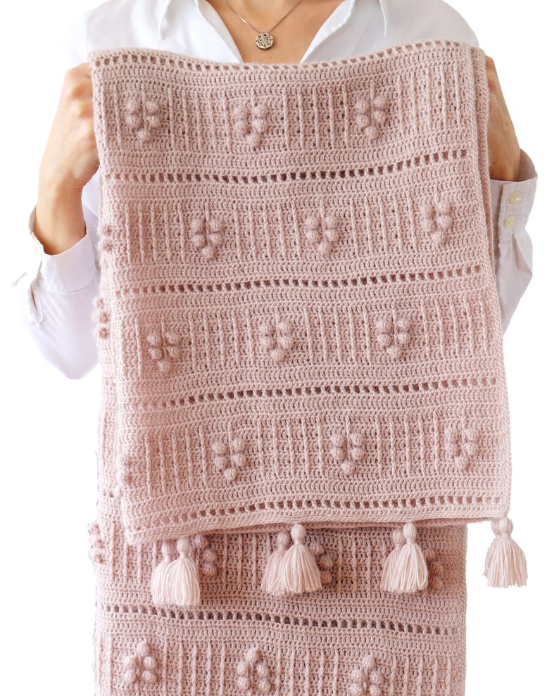 Peut inclure: Une couverture pour b&eacute;b&eacute; en crochet rose avec un motif textur&eacute; et des pompons sur les bords.