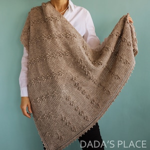 May include: A brown crocheted shawl with a textured pattern and a scalloped edge. The shawl is draped over a person's shoulders.