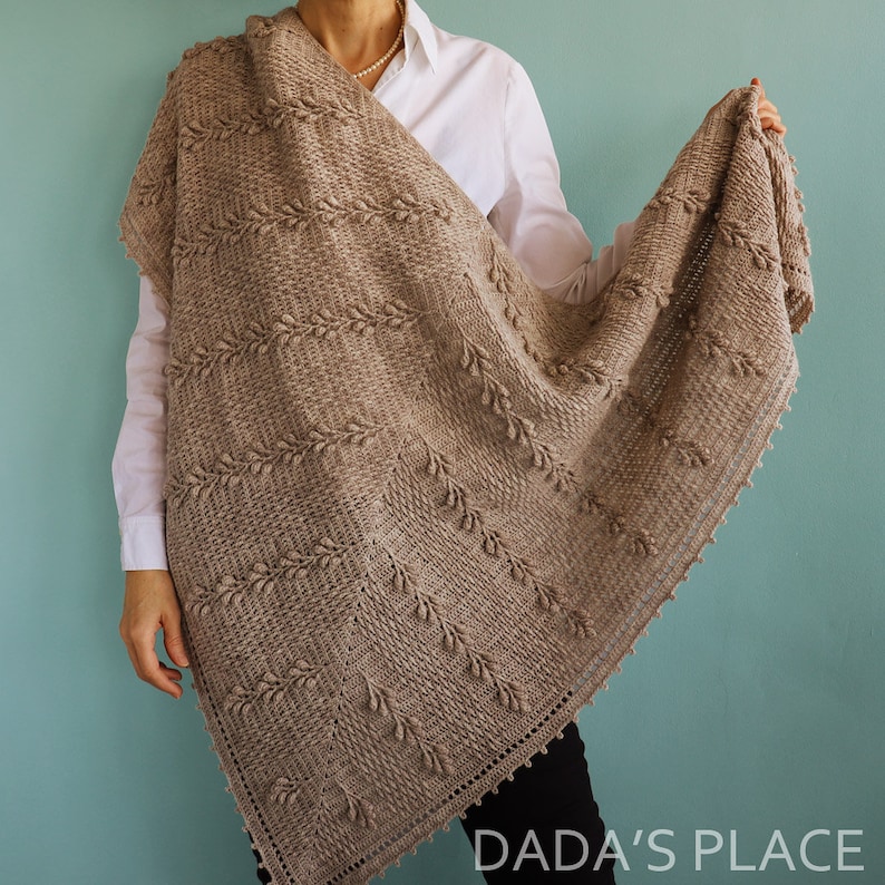 May include: A brown crocheted shawl with a textured pattern and a scalloped edge. The shawl is draped over a person's shoulders.