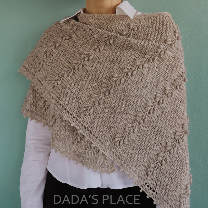 May include: A beige crochet shawl with a leaf pattern and a scalloped edge. The shawl is draped over a person's shoulders.