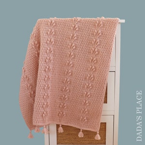 May include: A soft pink crocheted throw blanket with a textured leaf pattern and tassels on the edges.