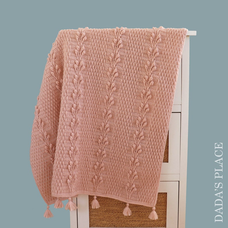 May include: A soft pink crocheted throw blanket with a textured leaf pattern and tassels on the edges.