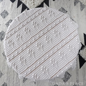 May include: A white crocheted blanket with a textured pattern of small raised dots. The blanket is circular and has a delicate, lacy look.