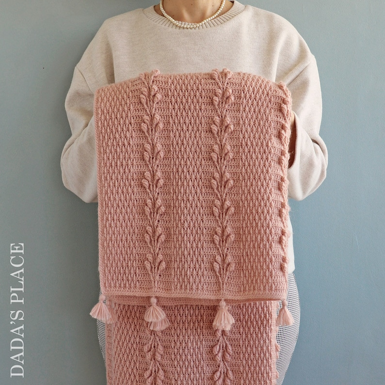 May include: A pink crocheted baby blanket with a leaf pattern and tassels.