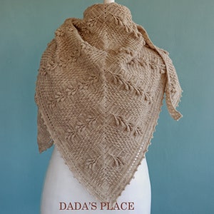 May include: A beige crocheted shawl with a delicate leaf pattern and fringe trim. The shawl is draped over a white mannequin.
