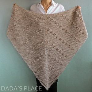 May include: A beige crocheted shawl with a delicate leaf pattern and a scalloped edge. The shawl is draped over a person's shoulders.
