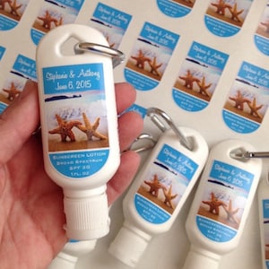 May include: White plastic sunscreen lotion bottles with a keychain ring. The bottles have a blue and white label with a picture of two starfish on a beach. The label also includes the text "Stephanie & Anthony June 6, 2015".