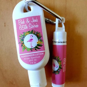 May include: White sunscreen lotion bottle and pink lip balm tube attached to a silver carabiner. The sunscreen bottle has a pink label with a flamingo illustration and the text "Bob & Jen's 65th Soirée". The lip balm is also pink with the text "65th Soirée".