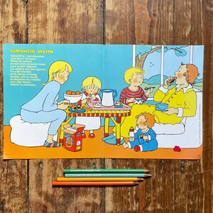 Op de afbeelding: Een vintage illustratie getiteld "DIMANCHE MATIN" toont een gezin aan het ontbijt. Een vrouw in een blauwe pyjama zit met kinderen, terwijl een man in gele vrijetijdskleding eet. Kleurpotloden zijn onder de illustratie gerangschikt.