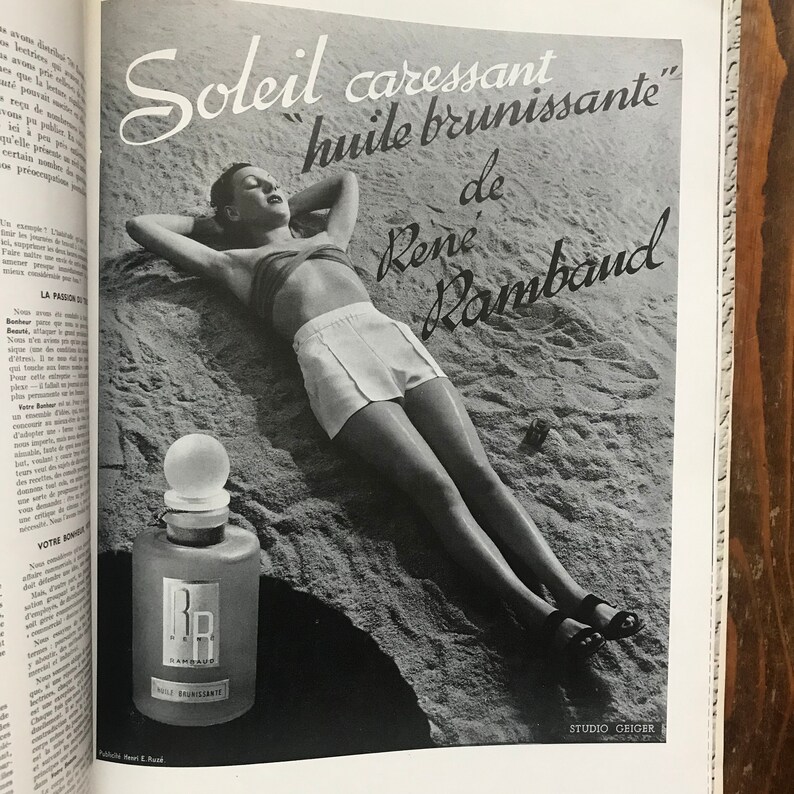 Pu&ograve; includere: Pubblicit&agrave; vintage in bianco e nero con una donna che prende il sole sulla spiaggia. L'annuncio include il testo "Soleil caressant huile brunissante de Ren&eacute; Rambaud" e una bottiglia di olio con le iniziali "RR".
